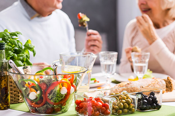A.Vogel: Spurenelement, Pillen sind kein Ersatz für gesunde Kost (Foto: 123RF, K. Bialasiewicz) Ein frischer knackiger Salat und Antipasti stehen auf einem Tisch. Ein älteres Paar geniesst das Essen im Hintergrund.