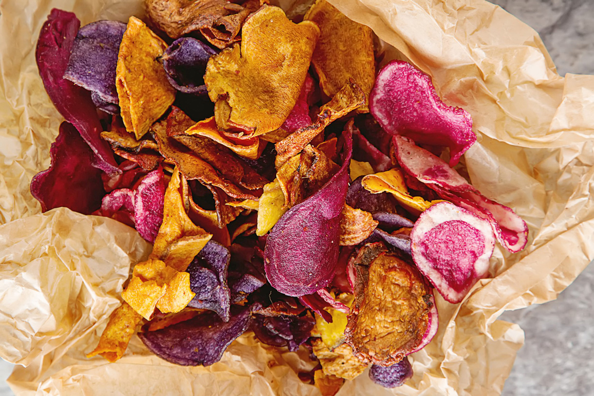 Diverses chips de légumes sont prêtes sur un morceau de papier sulfurisé.