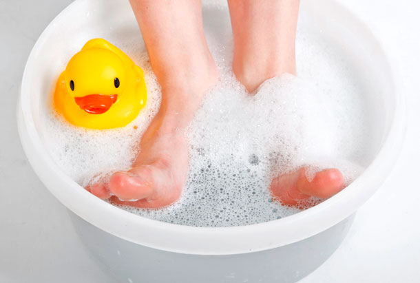 Fussbäder, Hydrotherapie (Foto: 123RF, jhandersen) Jemand entspannt seine Füsse in einer Schale Wasser mit Schaum und einer kleinen gelben Badeente.