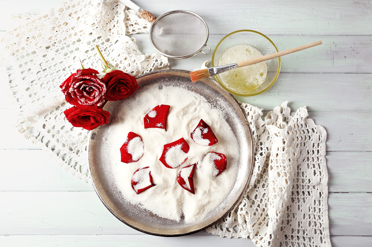 Essbare Blüten kann man kandieren und dann geniessen. (Foto: 123RF, serenzniy) Die Zutaten zum kandieren von Blüten sind schön drapiert auf einem wiesen Holztisch. Rosenblüten, Zucker und Eiweiss.