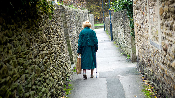 Besonders von Armut betroffene Menschen vereinsamen leicht. (Foto: agefotostock) Eine alte Dame spaziert alleine einen Weg entlang.