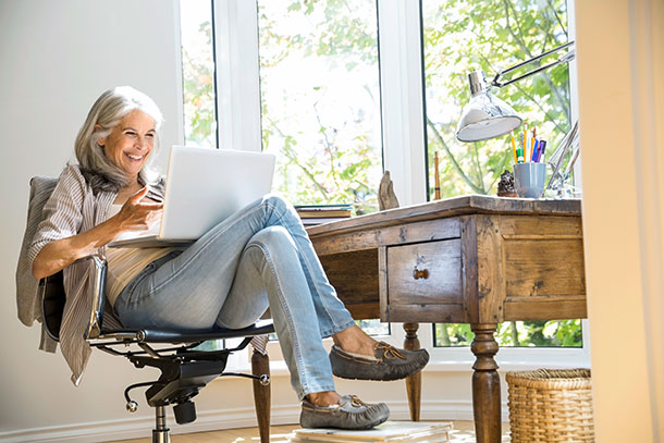 Nette Kontakte lassen sich auch über Internet-Plattformen finden. (Foto: agefotostock) Eine Frau sitzt lachend vor einem Laptop.