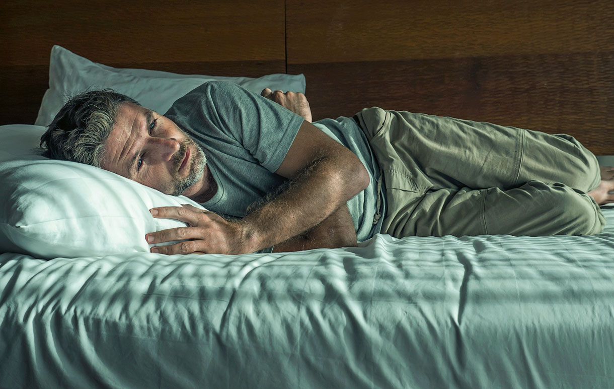Un homme est allongé dans son lit et semble avoir du mal à s'endormir.