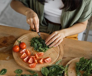 Ernährungstipps bei Hitzewallungen (Foto: 123RF, sofiiashunkina) Man sieht aus der Vogelperspektive eine Frau mediterranes Gemüse und Kräuter schneiden. Tomaten, Rucola, Kresse und ihre Hände sind zu sehen.