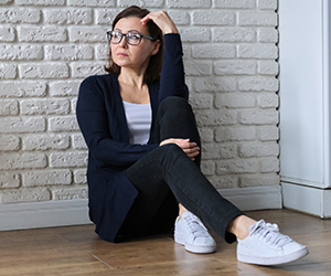 Ängste in den Wechseljahren (Foto: 123RF, photolight2) Eine reife Frau sitzt, an eine Wand gelehnt, auf dem Fussboden und sieht nachdenklich in die Ferne.