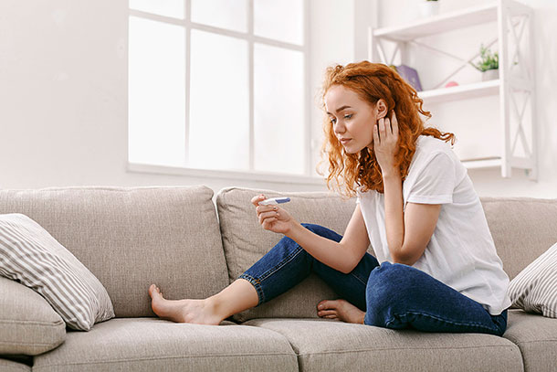 Chlamydien: Laut Experten sind nicht entdeckte Chlamydien-Infektionen die häufigste Ursache für ungewollte Kinderlosigkeit. (Foto: 123RF, Milkos) Eine junge Frau sitzt auf dem Sofa und betrachtet einen Schwangerschaftstest in ihrer Hand.