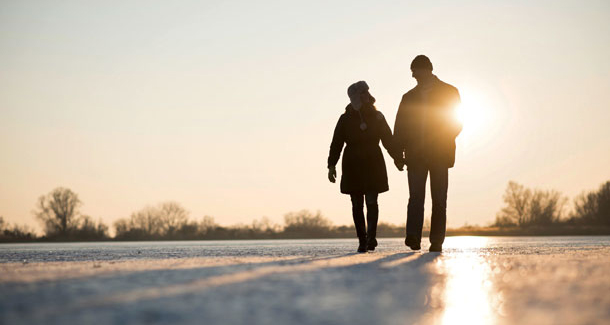 Ein Spaziergang nach dem Essen entlastet die Leber. (Foto: 123RF, martinan) Man sieht ein paar in verschneiter Landschaft beim Spaziergang. Der Sonnenuntergang färbt die Szene bereits in ein warmes Gelb.