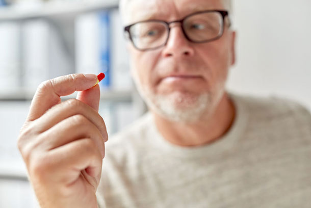 A.Vogel: Possibilités de traitement avec des substances synthétiques (Photo: 123RF, Dolgachov) Un homme regarde d'un œil critique une pilule qu'il tient dans sa main.
